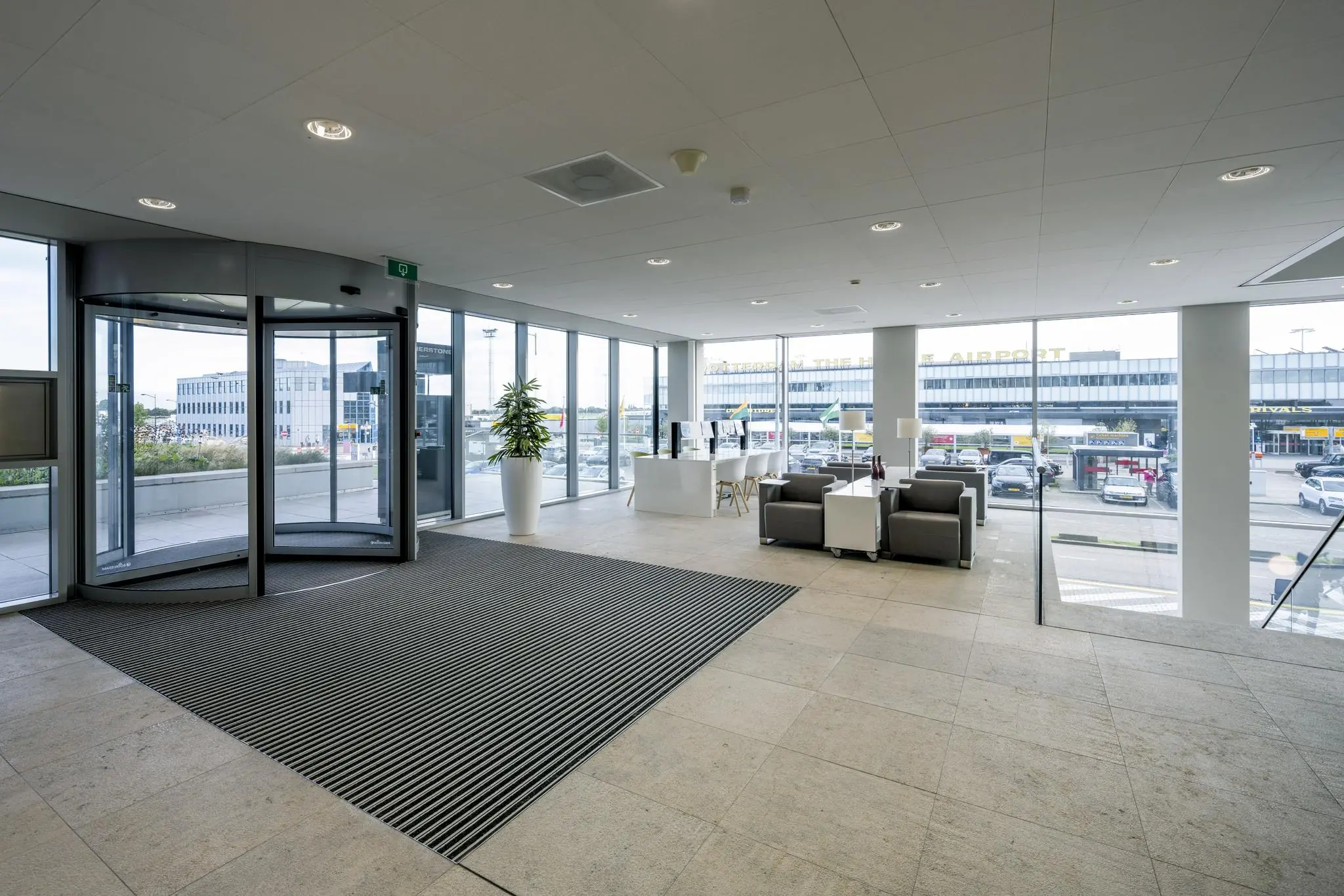 Inkomhal met zitgedeelte en glazen gevel met uitzicht op Rotterdam The Hague Airport.